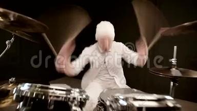 穿白色衣服的帅哥在黑色背景下积极地玩鼓套件。 特写